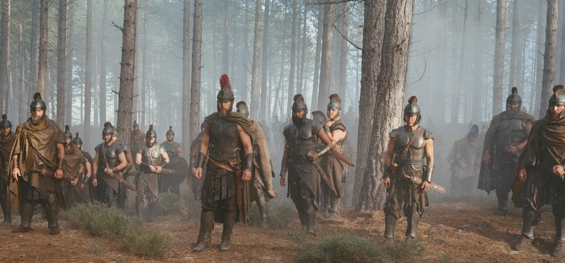 This image shows Matt Damon as Odysseus alongside his men in a misty pine forest scene from Christopher Nolan's epic film adaptation, The Odyssey (2026)