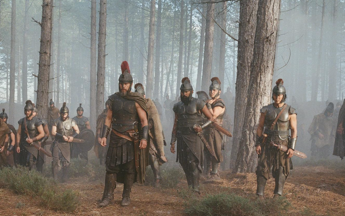 This image shows Matt Damon as Odysseus alongside his men in a misty pine forest scene from Christopher Nolan's epic film adaptation, The Odyssey (2026)